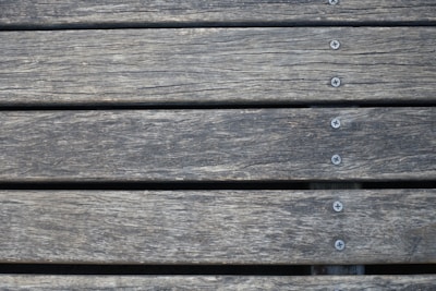 Wooden planks aligned horizontally, featuring a weathered texture with visible grain patterns. Several metal screws are evenly spaced along the center of each plank, securing them together.