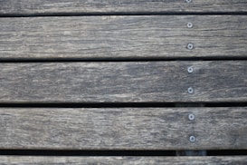 Wooden planks aligned horizontally, featuring a weathered texture with visible grain patterns. Several metal screws are evenly spaced along the center of each plank, securing them together.