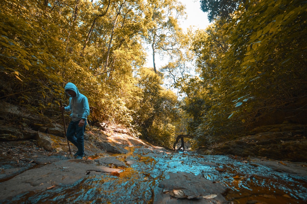 man in grey hoodie walking on creek with stick