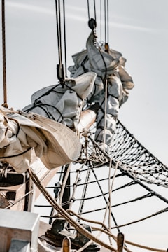 The image displays a close-up view of a ship's rigging, focusing on tightly coiled sailcloth, ropes, and a net against a clear sky. The wooden masts and lines are intricately detailed, showcasing the craftsmanship of nautical equipment.