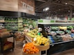 A well-organized produce section within a grocery store featuring a wide variety of fresh fruits and vegetables. The display includes items like oranges, bananas, lemons, and an array of leafy greens. The section is labeled 'Organic' and the signage emphasizes nutrition. The lighting is bright and the overall setup is clean and orderly.
