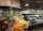 A well-organized produce section within a grocery store featuring a wide variety of fresh fruits and vegetables. The display includes items like oranges, bananas, lemons, and an array of leafy greens. The section is labeled 'Organic' and the signage emphasizes nutrition. The lighting is bright and the overall setup is clean and orderly.