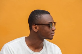 A person wearing glasses is seen in profile against a bright orange background. The individual is wearing a white shirt.