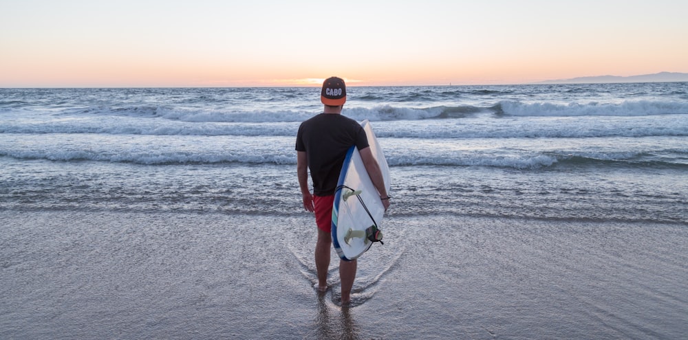 Persona de pie mientras lleva una tabla de surf mirando hacia el mar