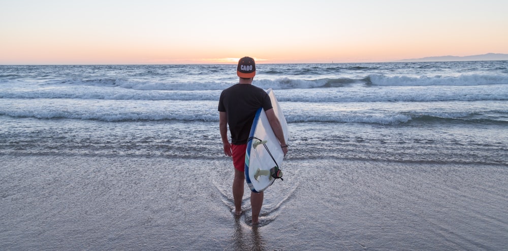 person standing while carrying surfboard facing sea