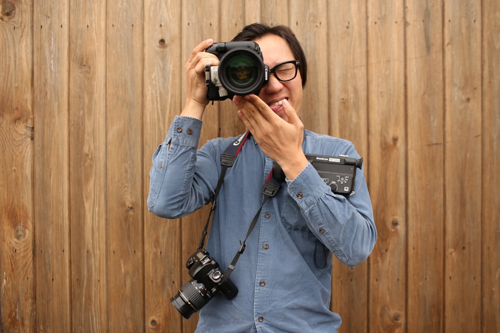 man standing beside wooden wall holding camera during daytime