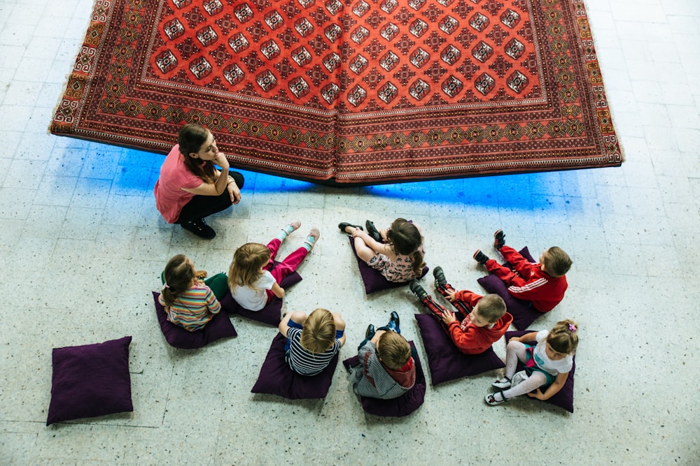 children and woman sitting on floor with pillows