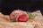 A raw piece of marbled beef is resting on crumpled brown parchment paper. Fresh rosemary sprigs and a few scattered red peppercorns add to the presentation. The meat is vibrant red with intricate patterns of white fat.