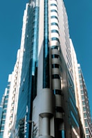 A modern, high-rise skyscraper with sleek architectural design features glass and concrete materials. The building is illuminated by natural sunlight, creating contrasting shadows and highlights.