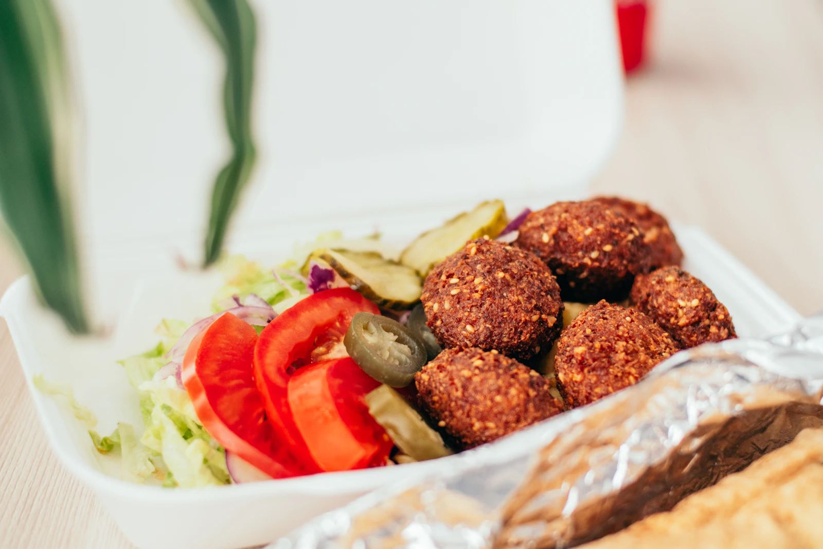 Golden fried falafel balls with sliced tomato, lettuce, pickles and flatbread in a takeaway box