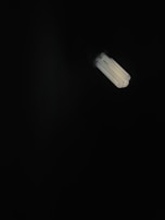 A fluorescent light bulb emits a soft glow in a dark environment, creating a stark contrast between the bright light and the surrounding darkness.