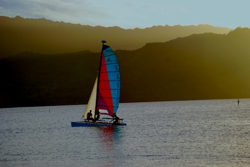 A sharp 2.4mR sailboat cutting through clear blue water with a vibrant sunset in the background