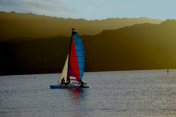 A vibrant sailboat with colorful sails gliding across a sparkling sea during sunset.