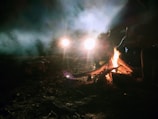 A campfire scene at dusk with tents and people gathered in the jungle.