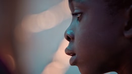 A close-up profile of a child looking intently forward with a soft focus and warm lighting creating a gentle glow on the face. The background is blurred with bokeh effects, adding to the dreamy atmosphere.