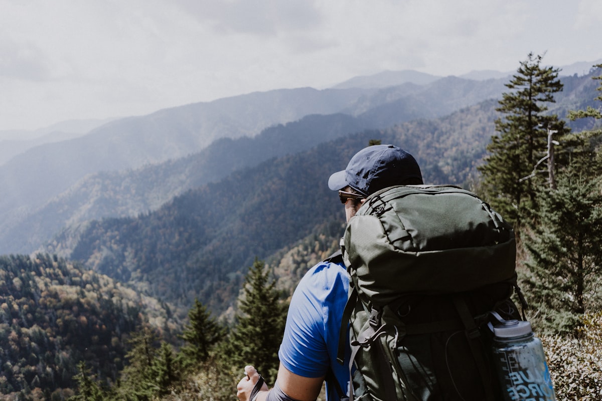 Hiker with a large green backpack looking out over layered forested Appalachian ridges fading into haze