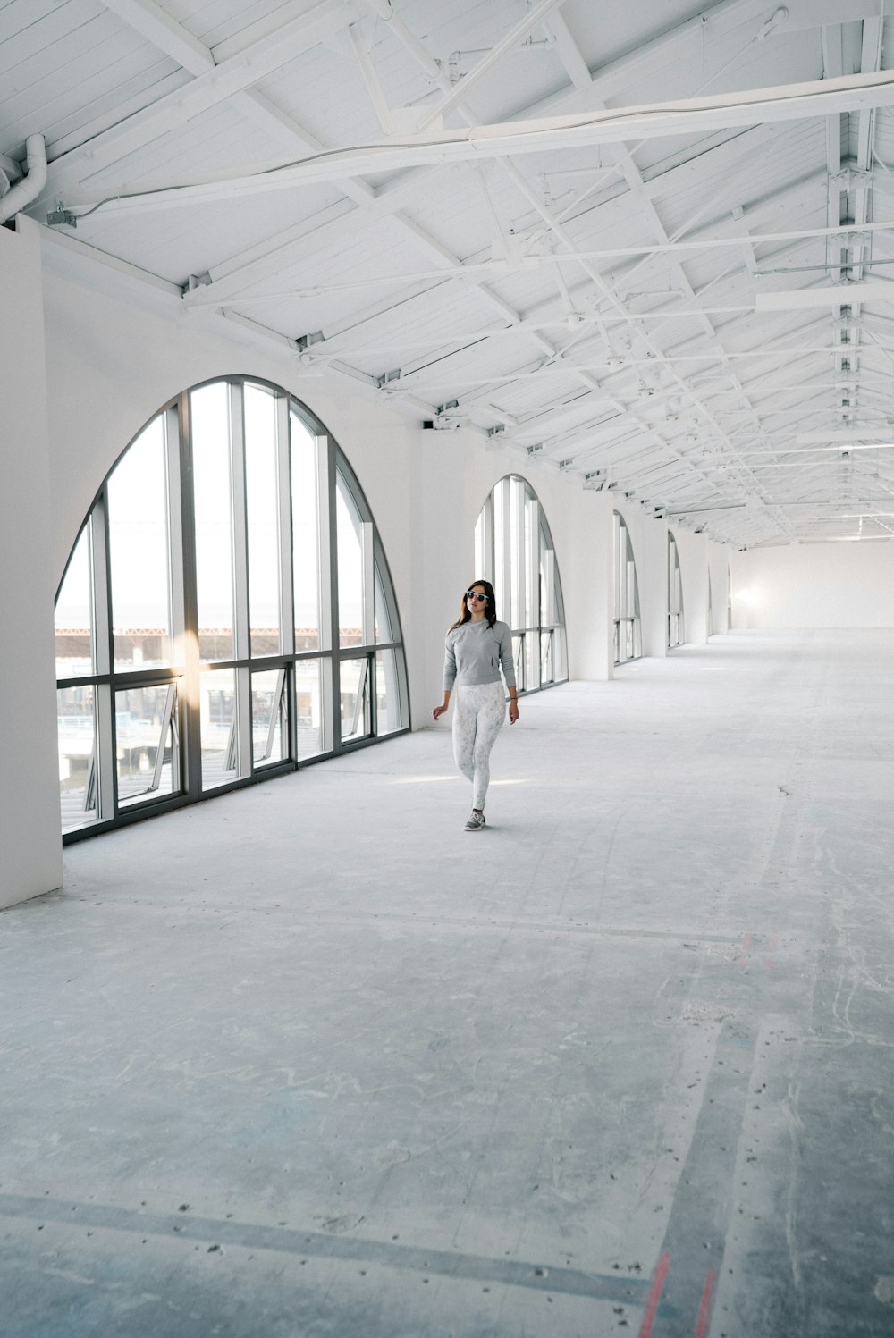woman walking on empty pathway near glass arch window