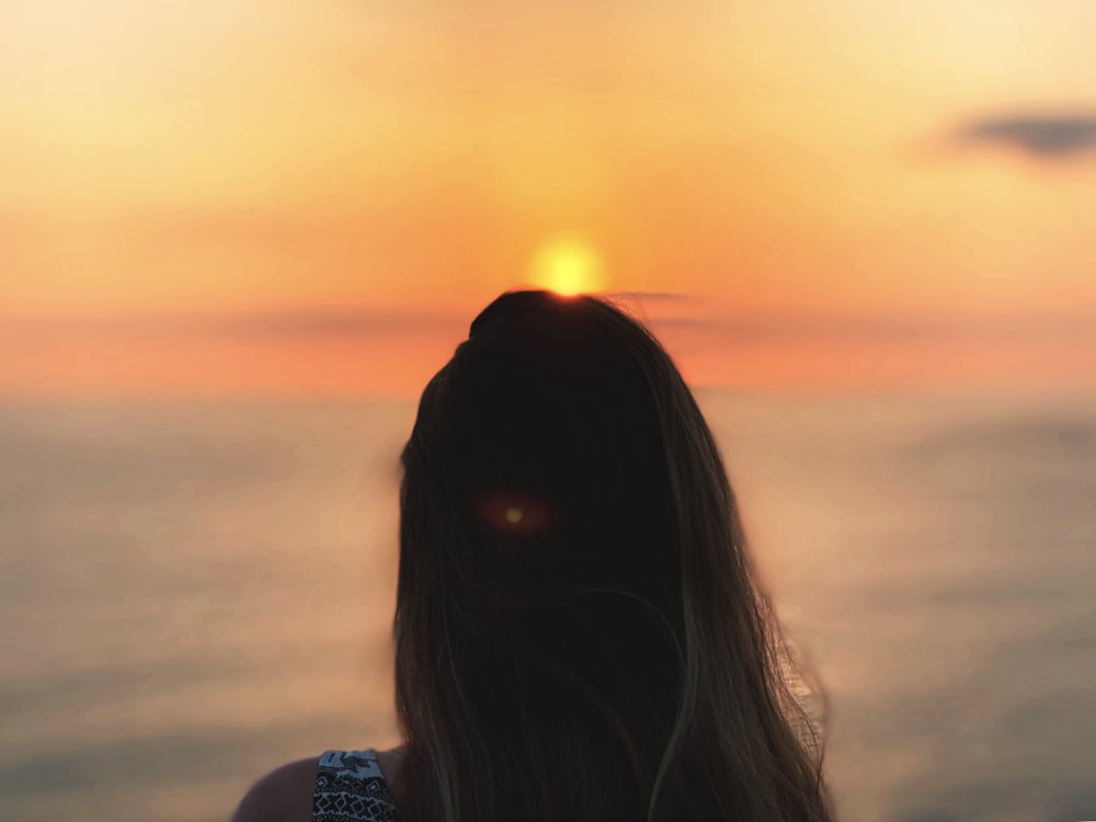 uma mulher olhando para o oceano ao pôr do sol
