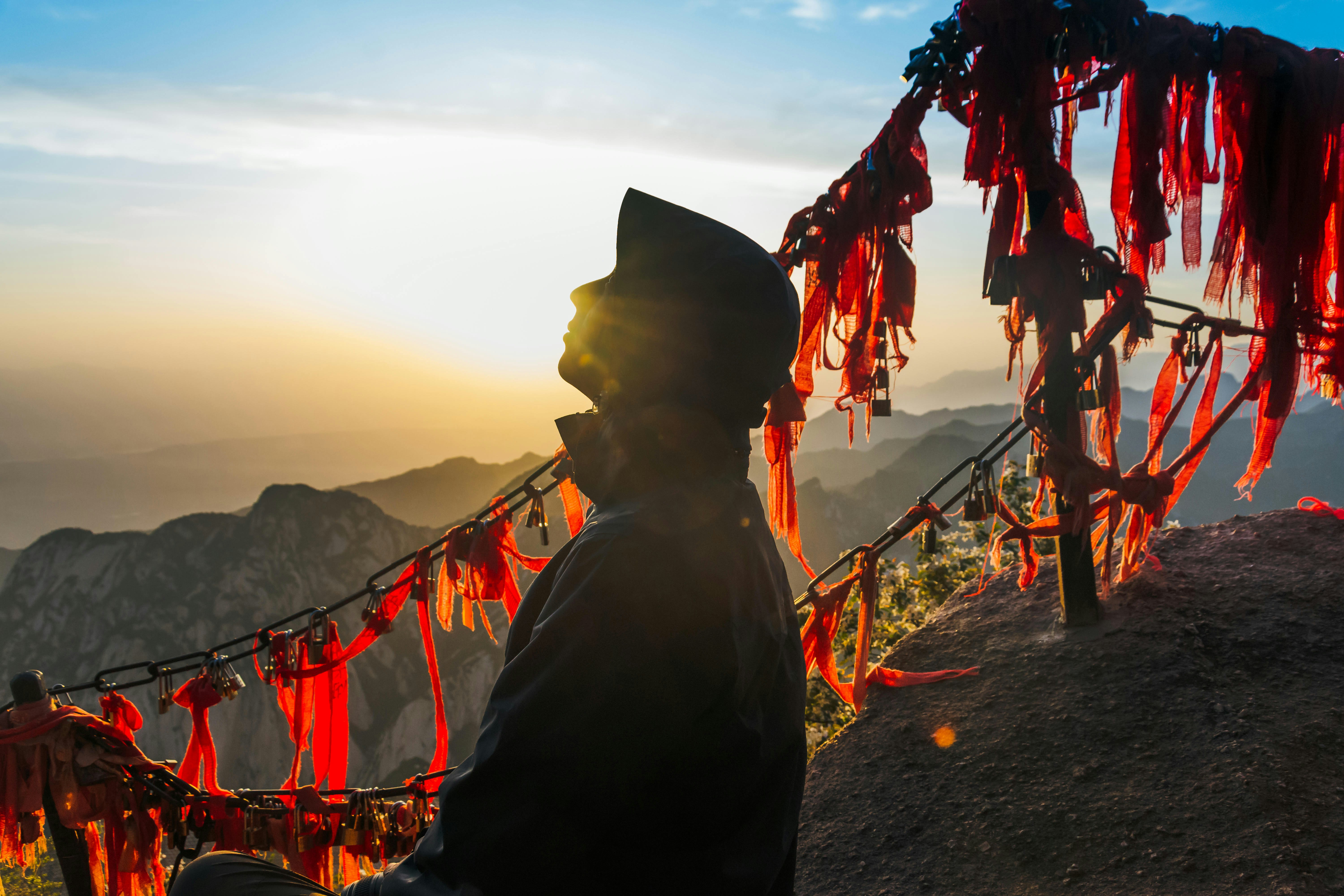 silhouette of man standing on cliff of mountain during sunset