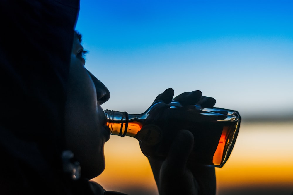 Persona bebiendo licor en botella de vidrio transparente