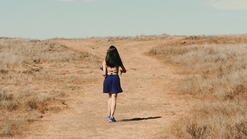 woman in blue dress walks on dirt road