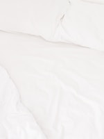 A neatly arranged bed with white sheets and pillows, conveying a sense of cleanliness and order. The fabric appears soft and inviting, suggesting comfort and relaxation.