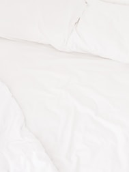 A neatly arranged bed with white sheets and pillows, conveying a sense of cleanliness and order. The fabric appears soft and inviting, suggesting comfort and relaxation.