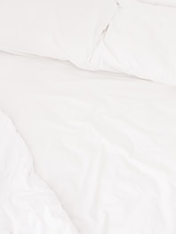 A neatly arranged bed with white sheets and pillows, conveying a sense of cleanliness and order. The fabric appears soft and inviting, suggesting comfort and relaxation.