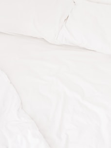 A neatly arranged bed with white sheets and pillows, conveying a sense of cleanliness and order. The fabric appears soft and inviting, suggesting comfort and relaxation.