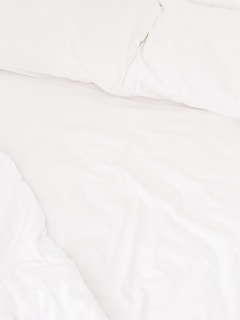 A neatly arranged bed with white sheets and pillows, conveying a sense of cleanliness and order. The fabric appears soft and inviting, suggesting comfort and relaxation.