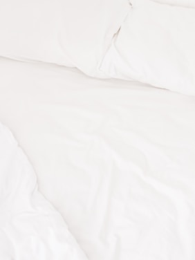 A neatly arranged bed with white sheets and pillows, conveying a sense of cleanliness and order. The fabric appears soft and inviting, suggesting comfort and relaxation.