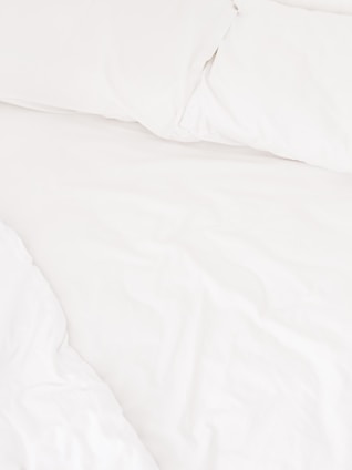 A neatly arranged bed with white sheets and pillows, conveying a sense of cleanliness and order. The fabric appears soft and inviting, suggesting comfort and relaxation.