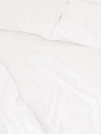 A neatly arranged bed with white sheets and pillows, conveying a sense of cleanliness and order. The fabric appears soft and inviting, suggesting comfort and relaxation.