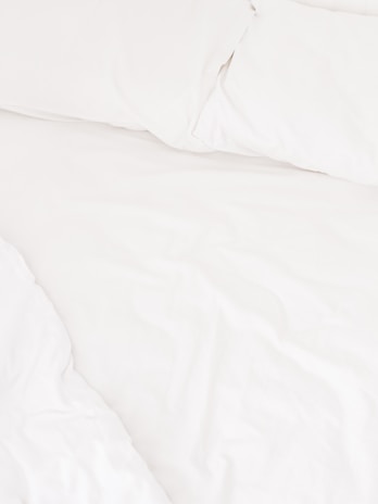 A neatly arranged bed with white sheets and pillows, conveying a sense of cleanliness and order. The fabric appears soft and inviting, suggesting comfort and relaxation.