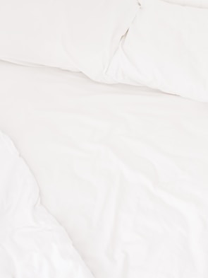 A neatly arranged bed with white sheets and pillows, conveying a sense of cleanliness and order. The fabric appears soft and inviting, suggesting comfort and relaxation.