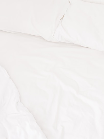 A neatly arranged bed with white sheets and pillows, conveying a sense of cleanliness and order. The fabric appears soft and inviting, suggesting comfort and relaxation.