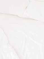 A neatly arranged bed with white sheets and pillows, conveying a sense of cleanliness and order. The fabric appears soft and inviting, suggesting comfort and relaxation.