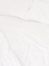 A neatly arranged bed with white sheets and pillows, conveying a sense of cleanliness and order. The fabric appears soft and inviting, suggesting comfort and relaxation.