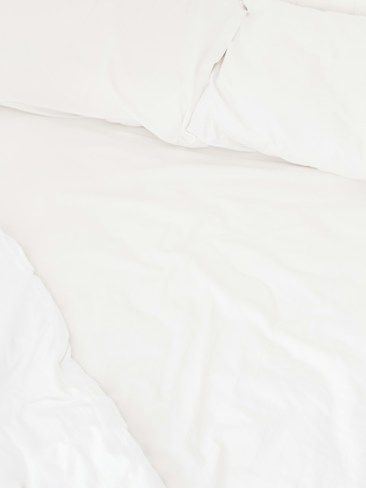 A neatly arranged bed with white sheets and pillows, conveying a sense of cleanliness and order. The fabric appears soft and inviting, suggesting comfort and relaxation.