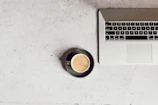 A sleek laptop open on a desk surrounded by notebooks and a coffee cup.