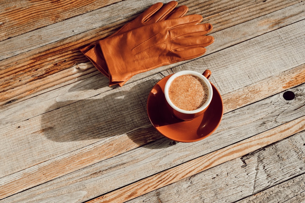 pair of brown leather gloves beside brown coffee cup