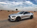 A sleek sports car parked on a cliff edge overlooking a vast desert landscape under a bright sky.