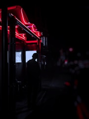 A shadowy figure in a vintage trench coat under flickering neon lights.
