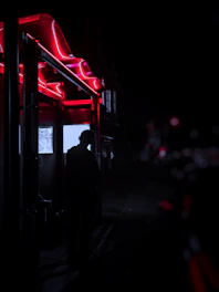 A shadowy figure illuminated by deep red neon lights in a mysterious urban alley.