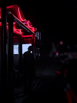 A shadowy figure in a vintage trench coat under flickering neon lights.