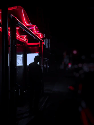A shadowy figure illuminated by deep red neon lights in a mysterious urban alley.