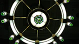 A large circular chandelier with stained glass decorations and illuminated bulbs. The design includes a central circular piece with intricate patterns and several smaller lights extending from the center, each featuring green and white stained glass.
