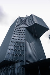 A modern skyscraper with a unique architectural design features a distinct honeycomb pattern on its facade. The building's exterior is made of glass and metal, giving it a sleek and futuristic appearance.