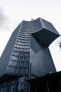A modern skyscraper with a unique architectural design features a distinct honeycomb pattern on its facade. The building's exterior is made of glass and metal, giving it a sleek and futuristic appearance.