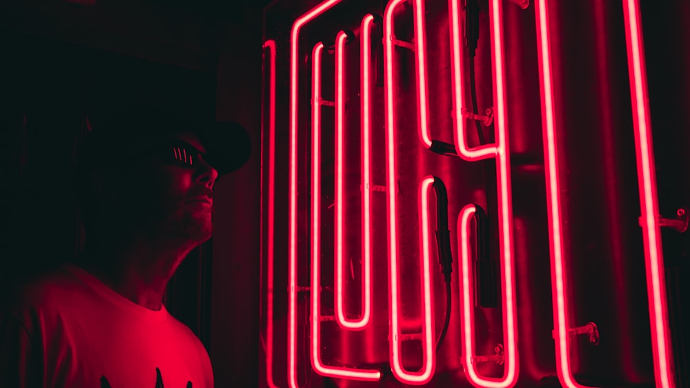 man stands beside red neon sign